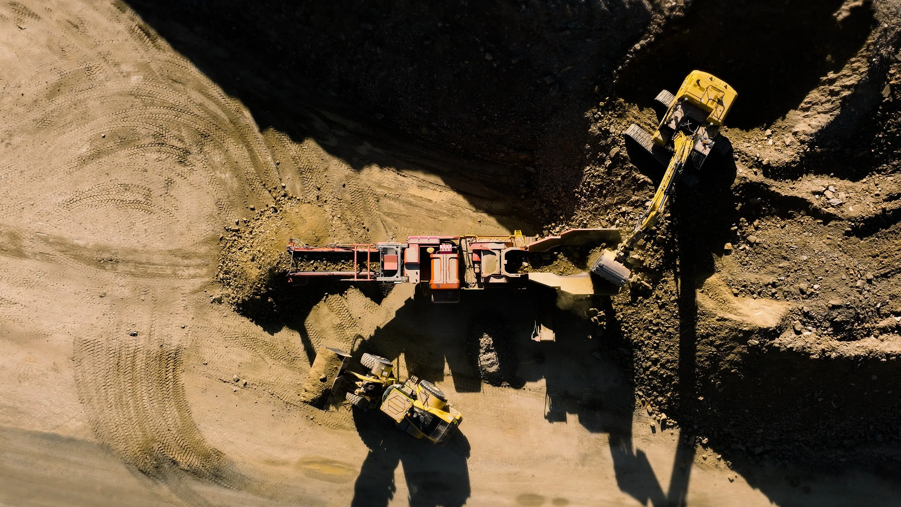 Looking straight down on an excavator feeding a mobile rock crusher, with a loader alongside, on the Eurobodalla Southern Storage Dam site